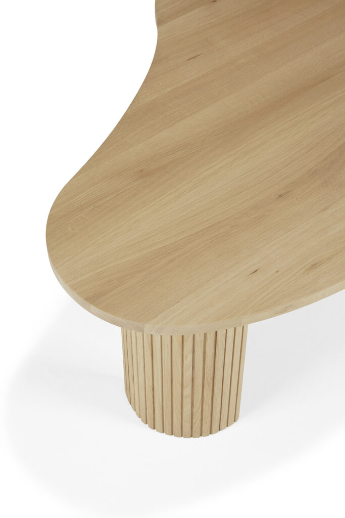 Gros plan d'une table basse en bois avec un plateau incurvé et un pied cylindrique nervuré. Le bois de chêne naturel a une finition claire et naturelle.