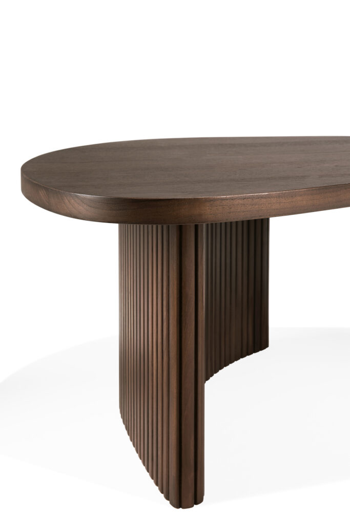 Une table ovale en bois de teck avec un plateau plat et une base constituée de lattes alignées verticalement, sur un fond blanc uni.