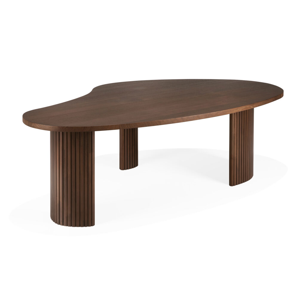 Une table basse en bois avec un plateau lisse et asymétrique ressemblant à un boomerang et trois pieds cylindriques présentant des rainures verticales.