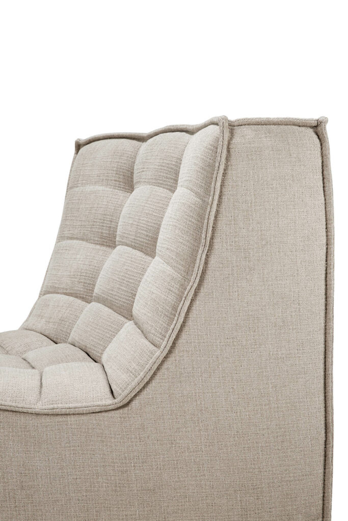 Gros plan d'un fauteuil en tissu beige avec un dossier rembourré et capitonné et des lignes simples et épurées, complétant parfaitement toute configuration de canapé modulaire avec son design à coins arrondis à 45°.