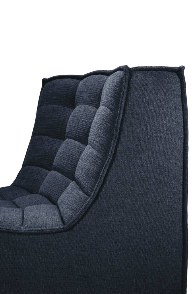 Gros plan d'une chaise en tissu matelassé bleu marine au design moderne et incurvé et au coin rond à 45°. Le revêtement présente un motif à carreaux avec un capitonnage profond, rappelant les détails complexes du canapé modulaire N701.