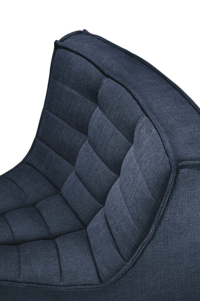 Vue rapprochée d'une chaise moderne rembourrée bleu foncé avec un dossier et une assise capitonnés et rembourrés, astucieusement positionnée à côté d'un canapé modulaire N701.