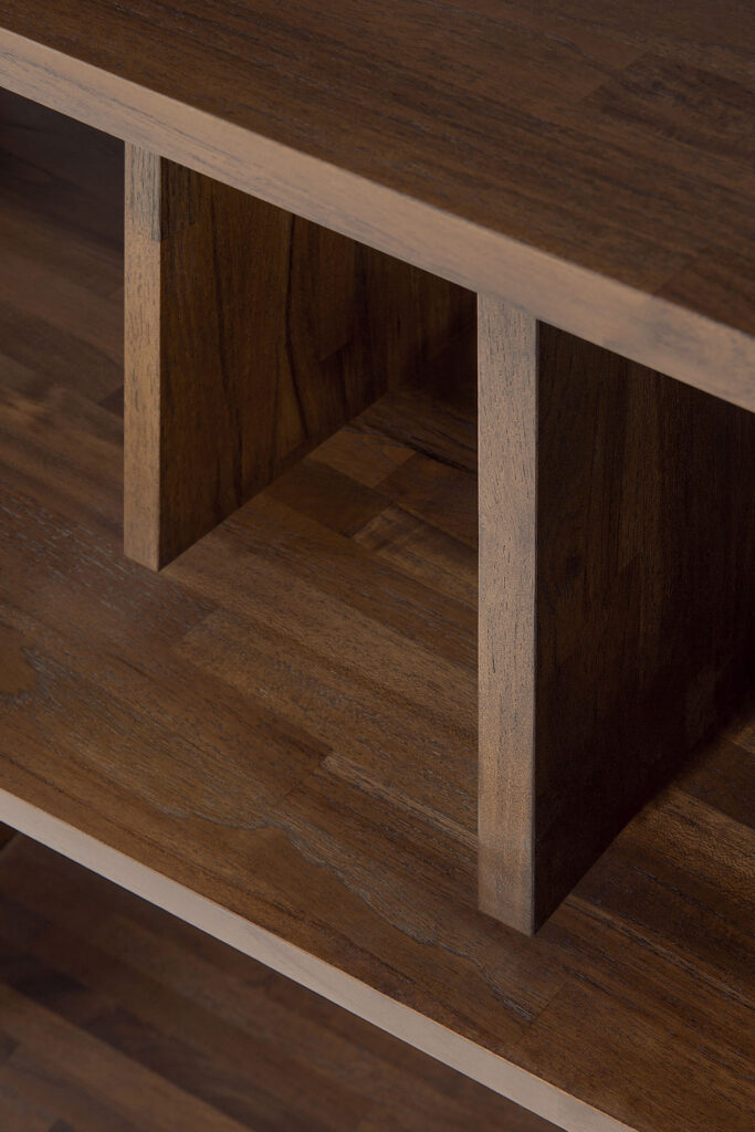 Vue rapprochée des étagères en bois d'un meuble, montrant le grain du bois de teck verni lisse et les séparateurs verticaux.