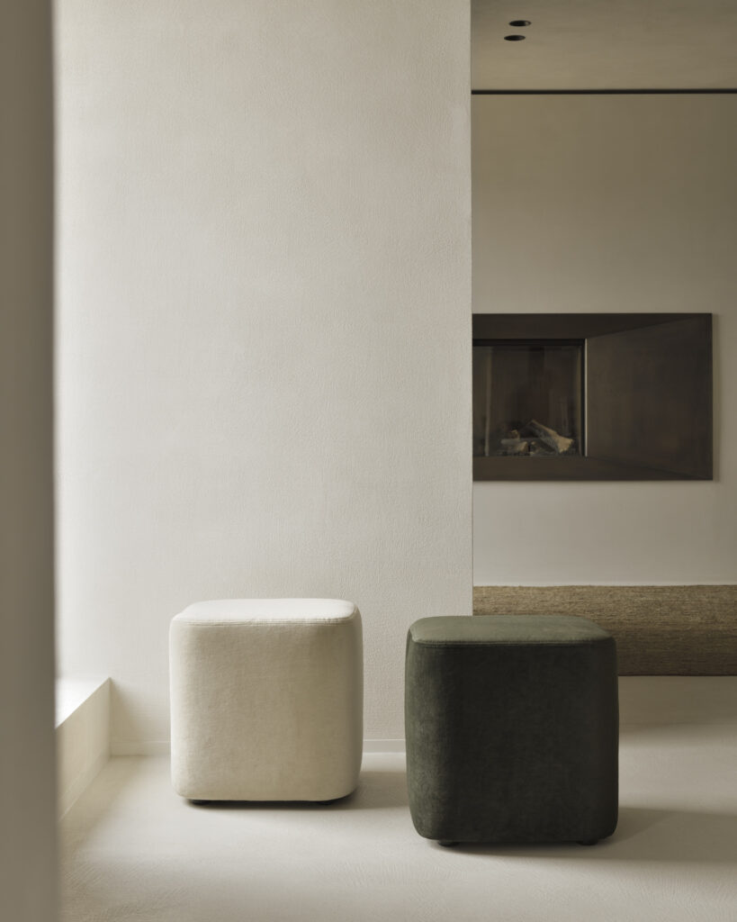 Deux poufs Cube - Tissu Cannelle, placés dans une pièce minimaliste avec des murs de couleur claire et une cheminée intégrée.