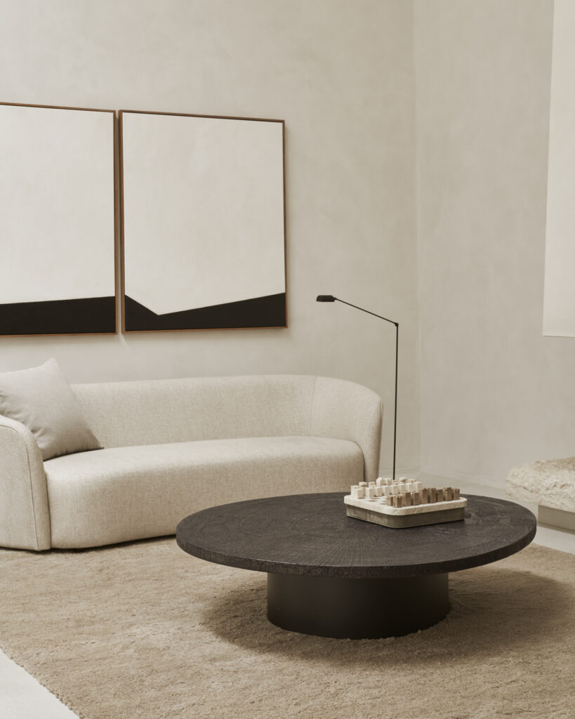 Salon moderne avec une table basse ronde noire, un canapé blanc, des œuvres d'art murales géométriques, un tapis beige et une décoration minimaliste.