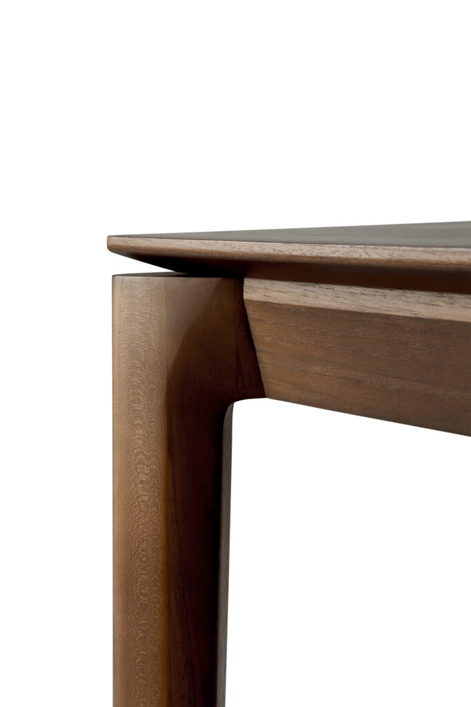 Gros plan d’un pied de table en bois moderne au design élégant et minimaliste. La table présente des lignes douces et inclinées et une finition teck teinté brun.