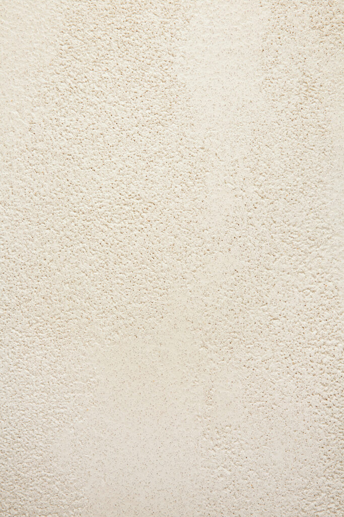 Gros plan sur une surface murale beige et texturée, à la finition rugueuse et irrégulière, évoquant l'attrait tactile des Table Elements fabriqués de manière artisanale.
