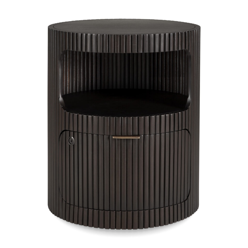 Le meuble à tiroirs Boomerang est une table de chevet ronde en bois foncé avec un design à lattes verticales, comprenant une étagère ouverte, un tiroir et une porte d'armoire avec une petite poignée.