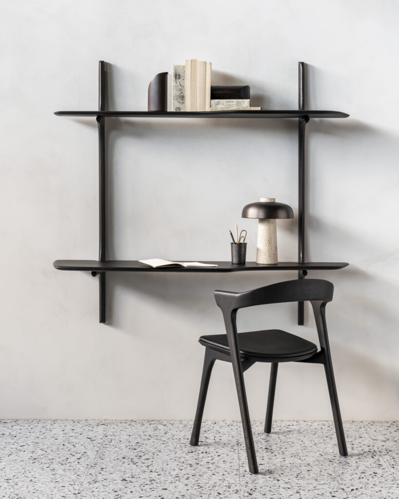 Un bureau mural PI noir minimaliste avec des étagères ouvertes contenant des livres et une lampe, associé à une chaise PI noire sur un sol en carrelage moucheté.