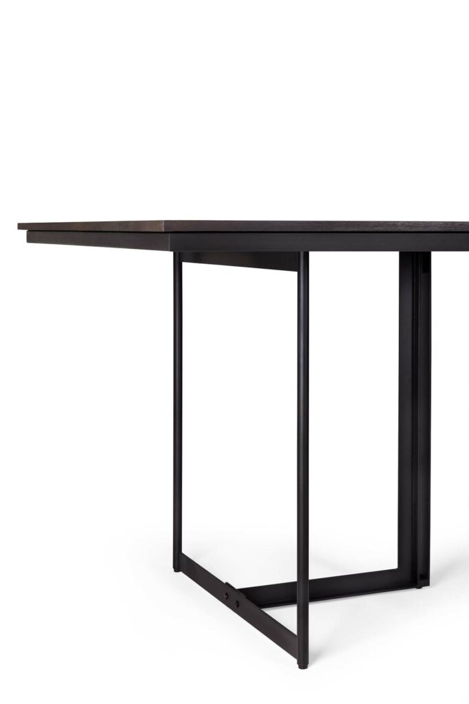 La table à manger Tacet présente un design minimaliste avec un cadre en métal noir et un plateau fin et plat.