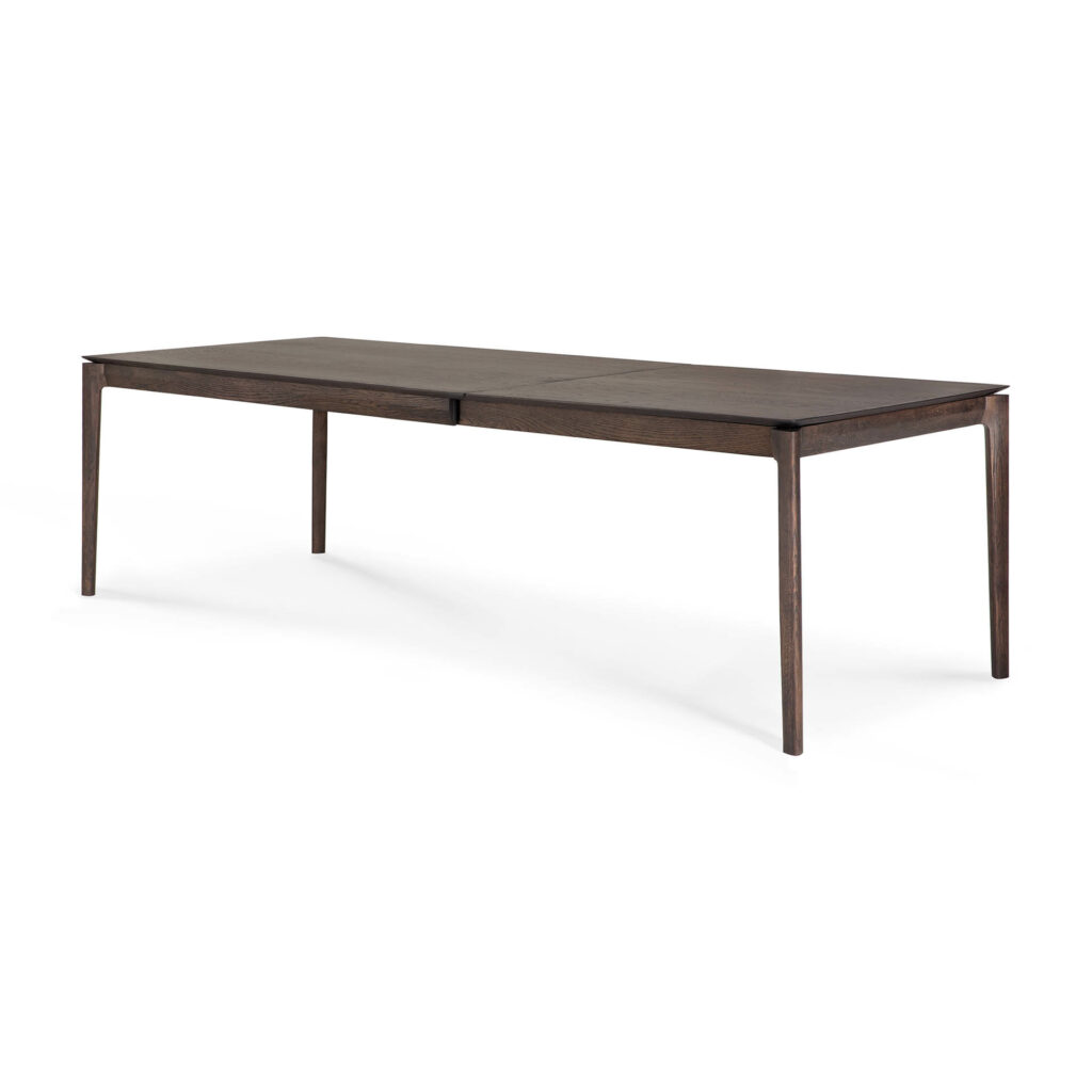 Une table à manger rectangulaire extensible en bois avec une finition foncée, dotée de pieds fins et d'un design élégant et minimaliste.
