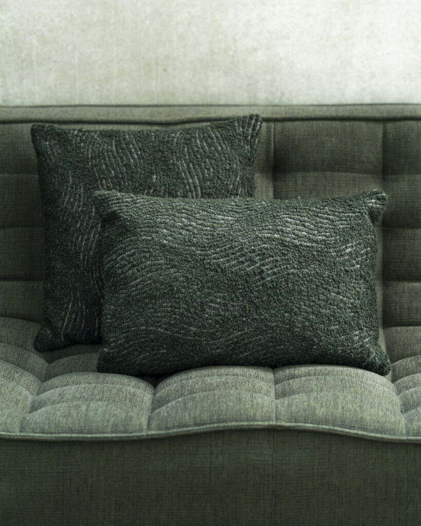 Deux coussins texturés Wave vert foncé sont placés sur un canapé capitonné vert assorti. Le mur derrière est gris clair.