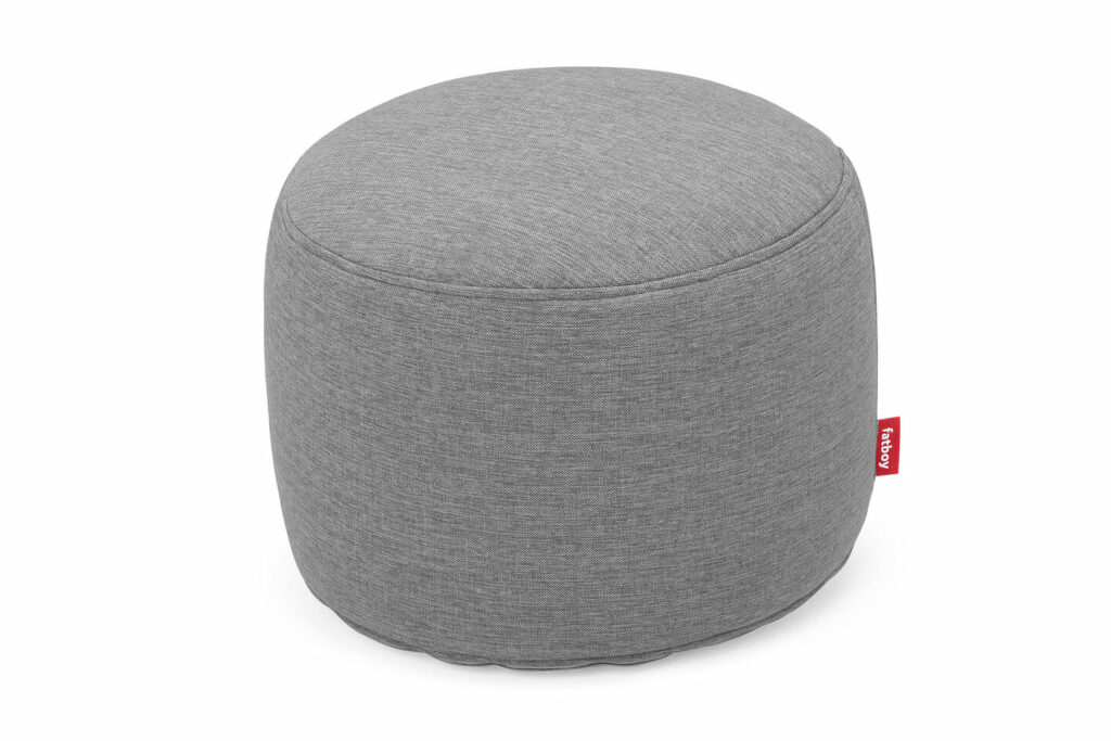 Pouf rond en tissu gris avec une petite étiquette rouge, idéal pour s'asseoir ou comme repose-pieds. Parfait pour une utilisation en extérieur, ce meuble Fatboy est polyvalent et élégant.