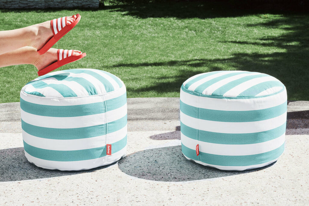 Deux poufs Fatboy à rayures vertes et blanches sur une terrasse. Les jambes d'une personne portant des sandales rouges et blanches sont visibles sur le côté gauche, posées de manière détendue, parfaites pour un décor extérieur.