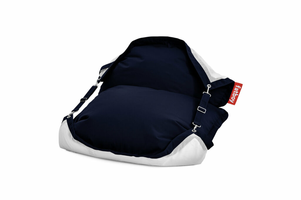Un grand pouf Fatboy bleu marine et blanc avec des sangles réglables et une étiquette rouge sur un côté, parfait pour se détendre au bord de l'océan sombre.