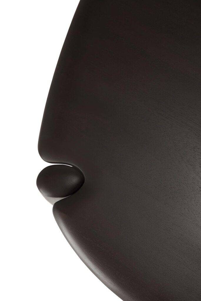 Gros plan d'une surface lisse et foncée d'Acajou teinté bron foncé avec une petite protubérance sphérique près du bord incurvé, rappelant la forme d'un galet.