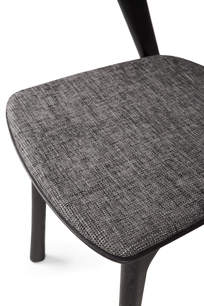 Gros plan d'une Chaise Bok avec pieds en chêne noir et assise rembourrée en tissu gris.