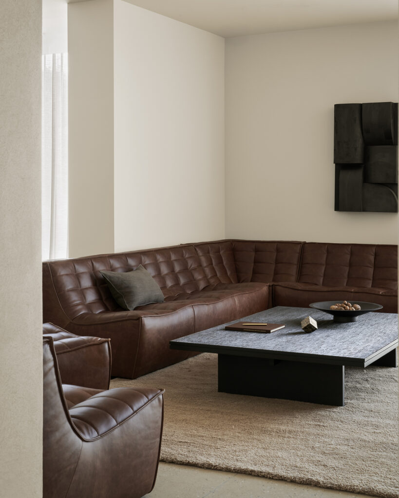 Un salon moderne est composé d'un canapé en cuir marron, d'un fauteuil assorti et de la Table basse Grooves comme pièce maîtresse, le tout disposé sur un tapis beige avec un décor neutre.