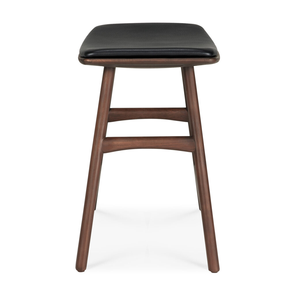 Le Tabouret Osso est un tabouret en bois avec un coussin d'assise en cuir noir, présentant un design simple avec deux barres de support horizontales entre les pieds.