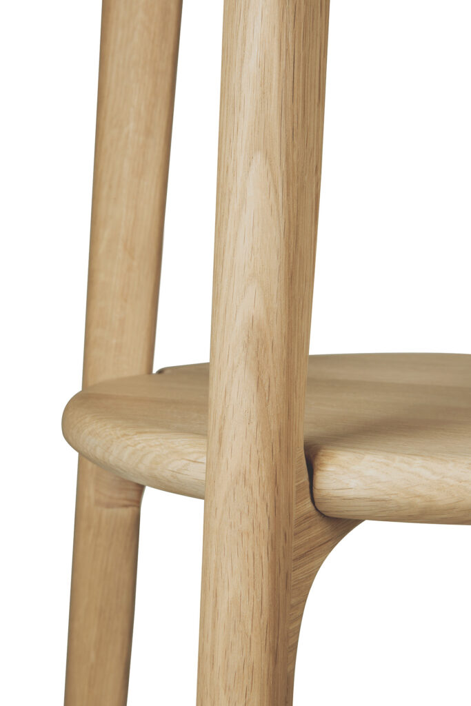 Gros plan d'une chaise en bois, montrant une partie de son siège rond et des pieds qui y sont reliés. Le grain du bois du chêne naturel est visible.