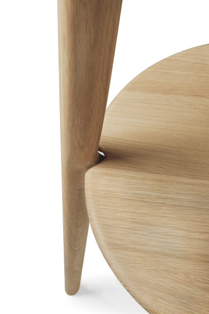 Gros plan d'un pied de table en bois intégré en douceur dans un plateau de table rond en chêne naturel huilé avec une texture de grain visible.