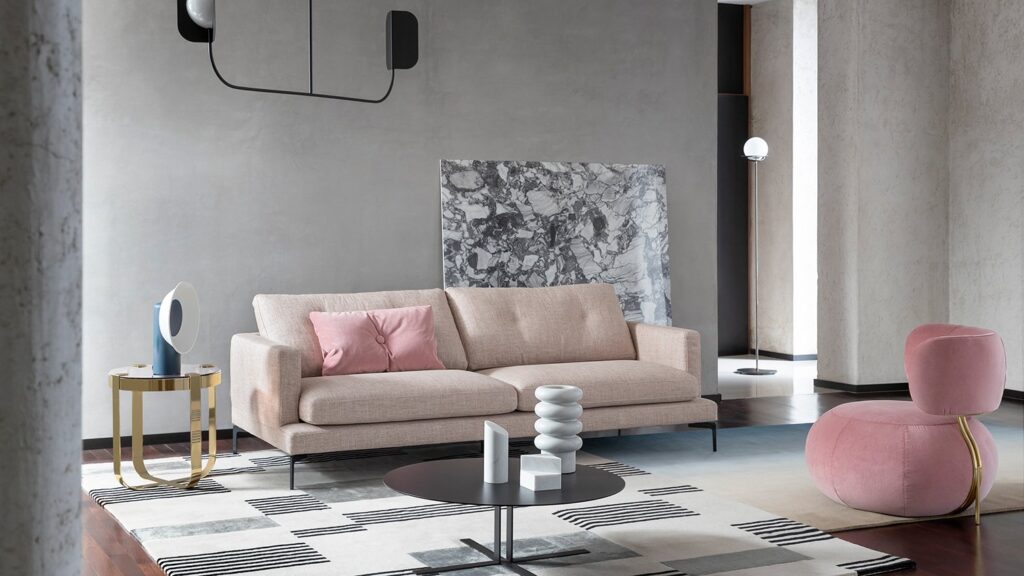 Un canapé beige, un fauteuil d'appoint rose, des tables rondes, un décor géométrique et un éclairage minimaliste sur des murs texturés gris - une inspiration parfaite pour votre espace.