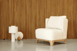 Un fauteuil blanc confortable, rappelant un canapé classique, est placé à côté d'une petite lampe blanche sur un sol clair, contrastant avec les tons chauds d'un mur en lattes de bois.