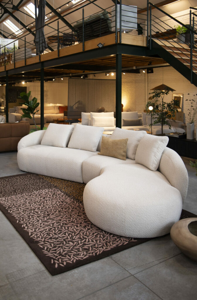 Un salon spacieux et moderne accueille un canapé Expo - Canapé Torino 2,5 places qui se marie parfaitement avec le grand canapé sectionnel blanc incurvé posé sur un tapis à motifs. Un loft de style industriel avec des balustrades en métal renforce l'ambiance chic en arrière-plan.