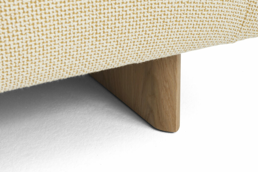 Gros plan d'un canapé 2 places Quilton Lift avec une base en chêne et un pied triangulaire en bois en tissu tissé beige sur une surface Tartaglia Ocre White.