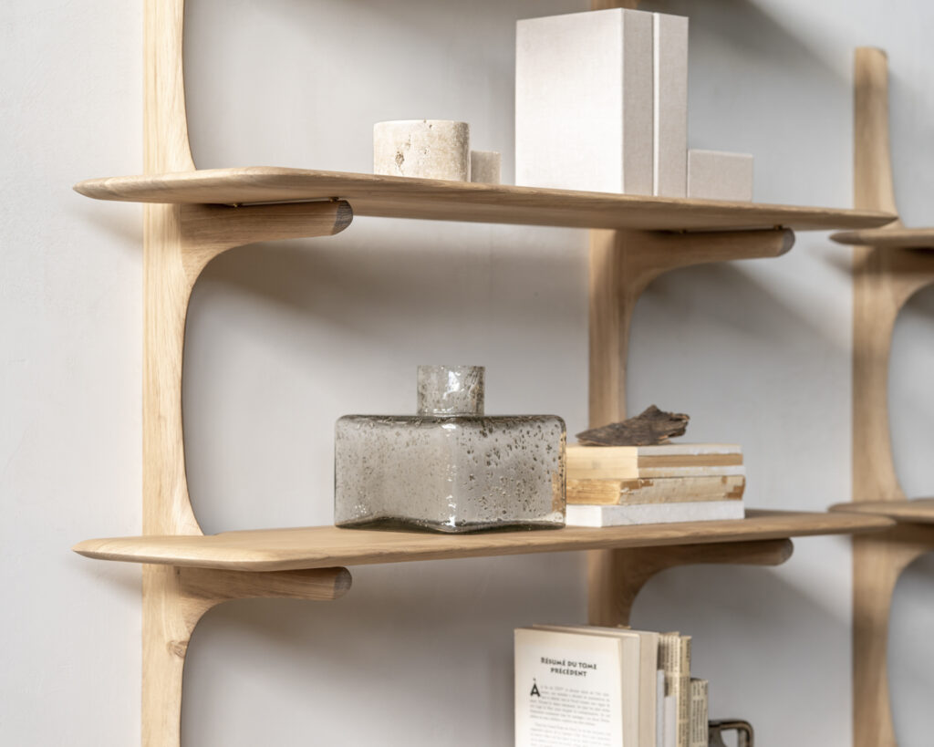 Étagère murale en bois avec trois étagères ornées d'objets décoratifs, dont un vase en verre, des livres et des objets cylindriques posés contre un mur uni, fabriqué en chêne naturel.