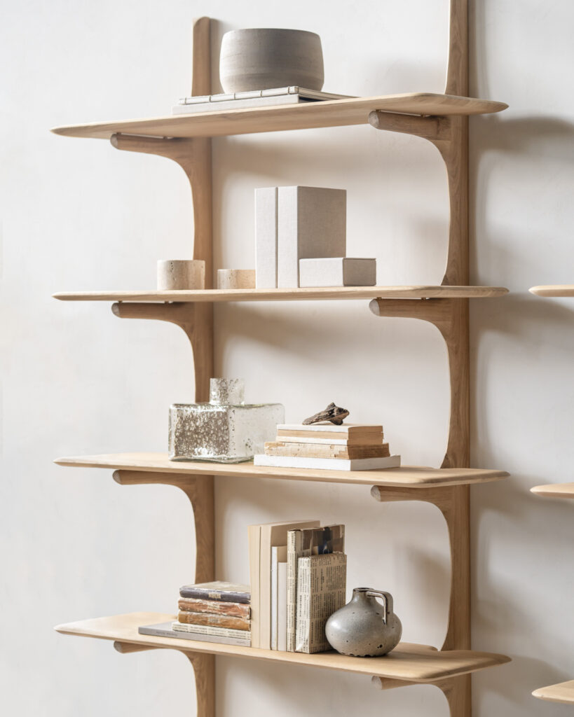 Une élégante étagère murale en chêne naturel est dotée de cinq étagères garnies de livres, de boîtes et d'objets décoratifs. Un charmant vase et des poteries complètent l'exposition contre le mur clair.