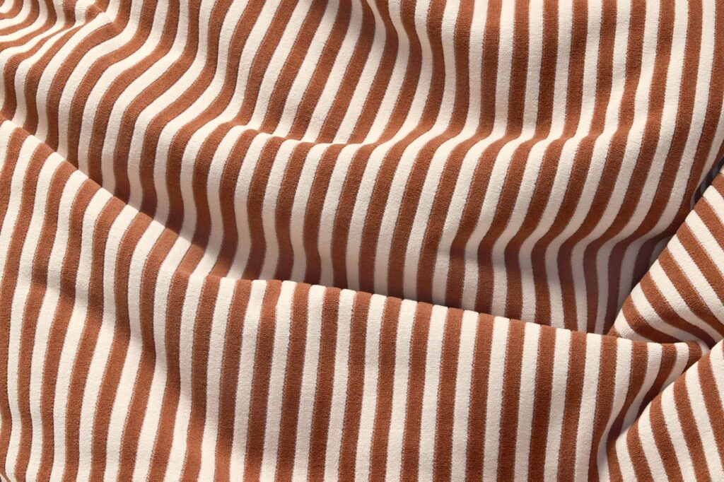 Le tissu présente des rayures marron et blanches avec des plis élégants, rappelant le style distinctif de Slim Terry Cognac.