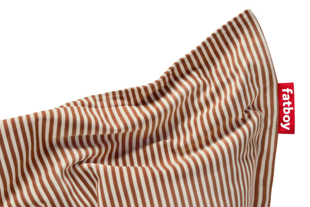 Gros plan d'un oreiller rayé beige et marron avec une étiquette rouge étiquetée « fatboy » sur le côté, infusé d'une touche de crème Blizzard Blue pour plus d'originalité.