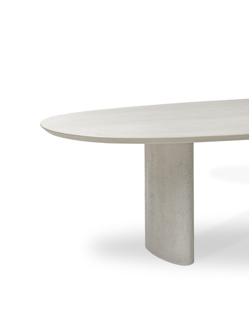 La table Ari est une table à manger minimaliste avec un bord arrondi et un support cylindrique, présentant une finition légère et texturée.