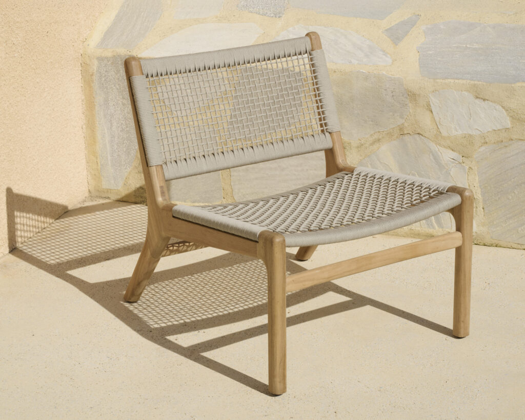 La chaise longue d'extérieur Jack Woven, posée contre un mur de pierre sur une terrasse ensoleillée, avec son assise et son dossier tissés, respire le charme.
