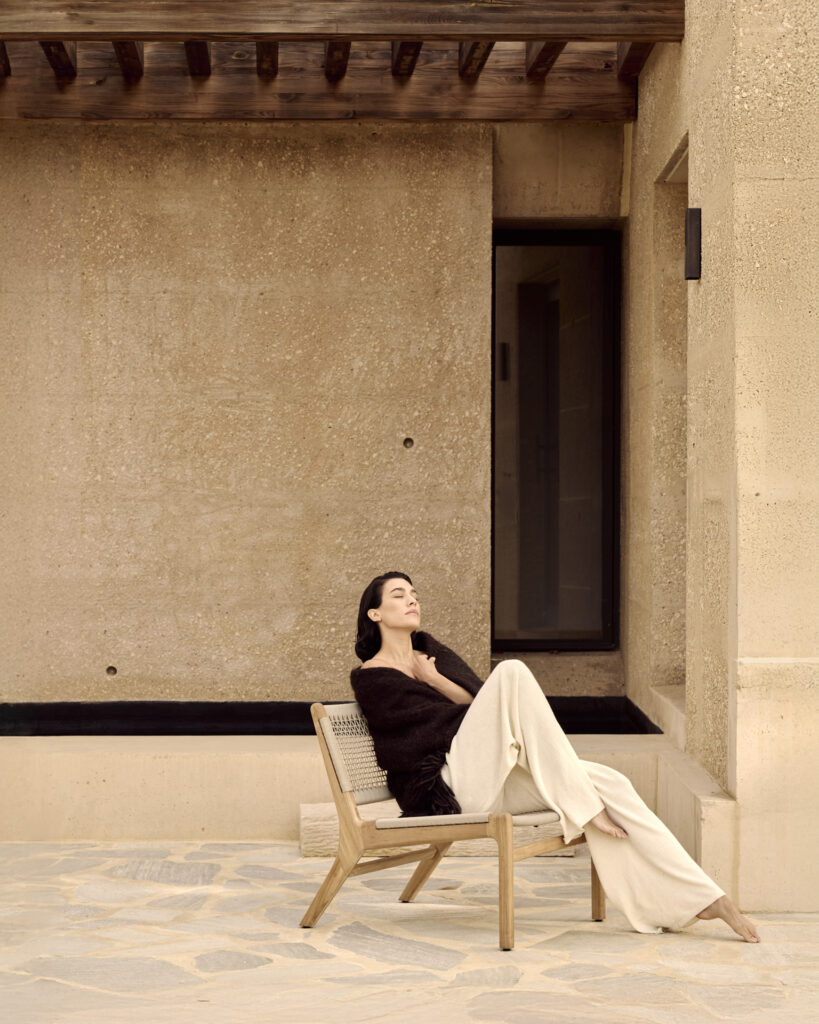 Une personne portant un haut foncé et un pantalon clair se détend les yeux fermés sur une chaise longue d'extérieur Jack Woven dans un cadre aux tons neutres.