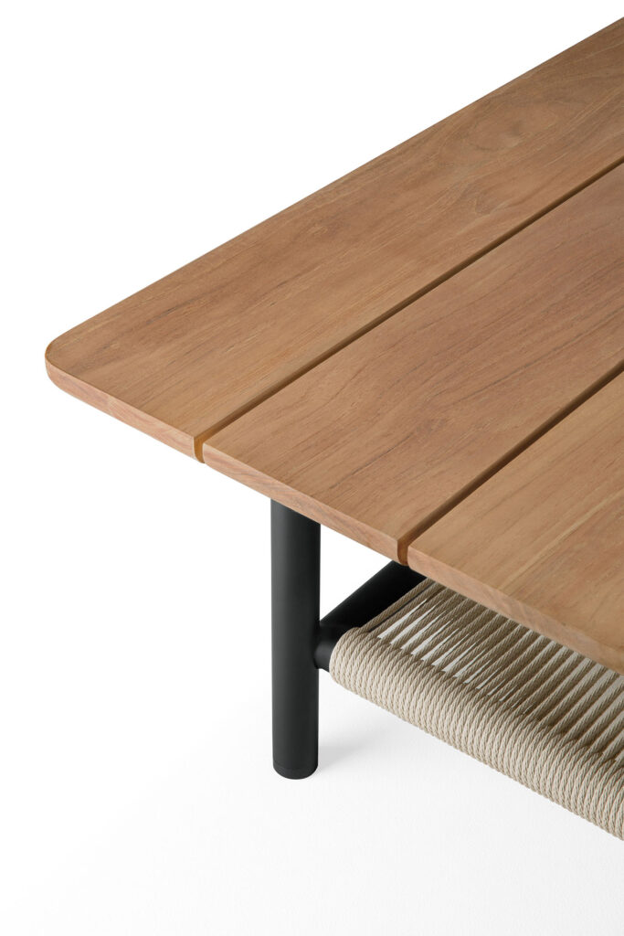 La table basse d'extérieur Corbey présente un design minimaliste avec des pieds en métal noir élégants, un coin en bois et une étagère en corde tressée sur un fond blanc immaculé. Elle est idéale pour les environnements intérieurs et extérieurs.