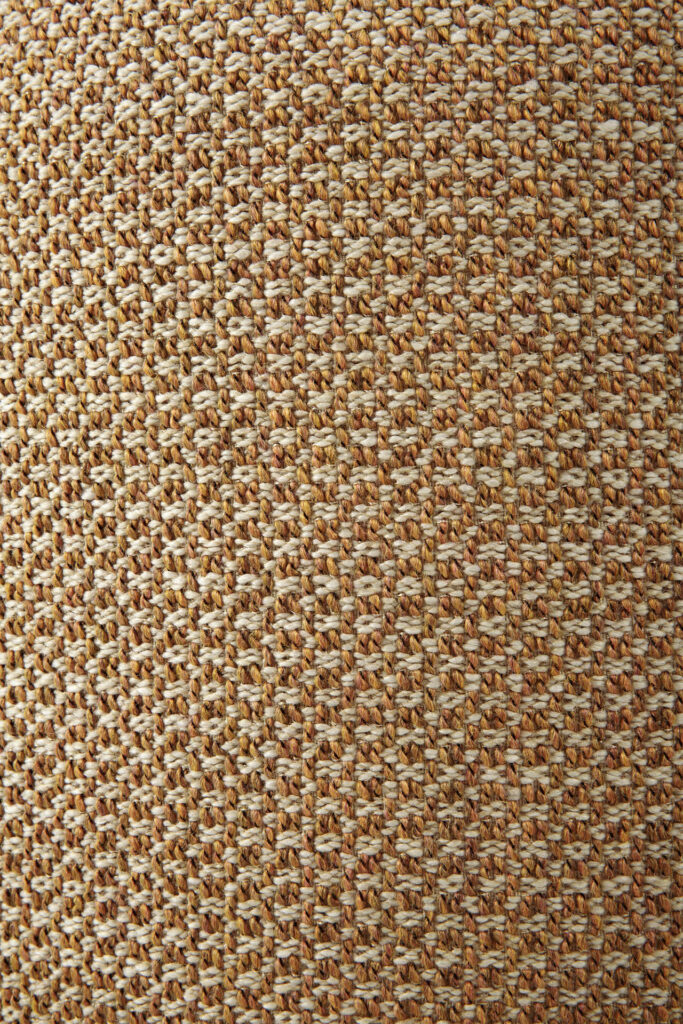 Gros plan d'un pouf de jardin avec une texture semblable à de la paille tressée, présentant un motif de brins entrelacés dans des tons naturels de marron et de beige.