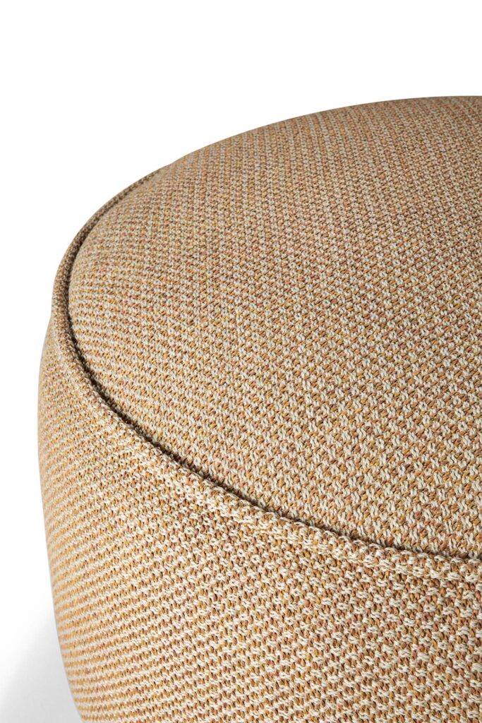 Gros plan d'un pouf rond en tissu de couleur beige avec une texture finement tissée, rappelant un beignet.