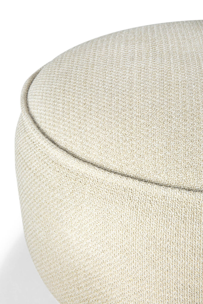 Gros plan d'un pouf rond, texturé beige clair, ressemblant à un beignet, avec une couture visible le long du bord supérieur.