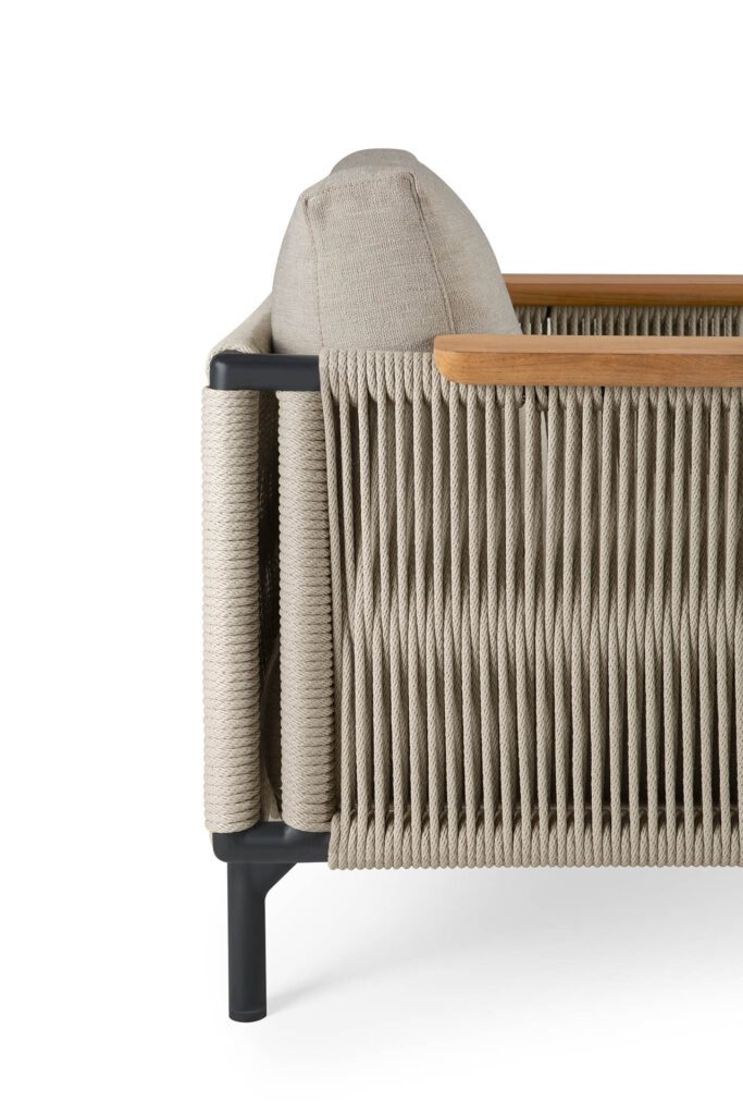 La chaise longue d'extérieur Corbey présente un design en corde tressée avec un coussin en tissu beige huître, complété par des pieds élégants en métal noir et un accoudoir en bois, offrant un profil latéral élégant.