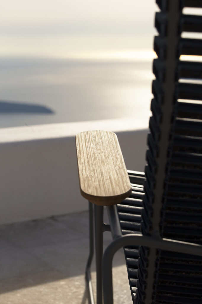 L'accoudoir en bois du transat CLICK est capturé en gros plan, sur fond de vues sereines sur la mer avec des îles lointaines et une douce lumière du soleil.