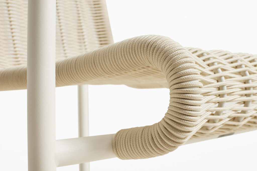 Gros plan d'un fauteuil Palissade CORD doté d'une assise en rotin tressé et d'accoudoirs gainés de tissu, dans des tons clairs et naturels. La structure arbore une finition blanc crème lisse et mate, qui souligne son élégante simplicité.