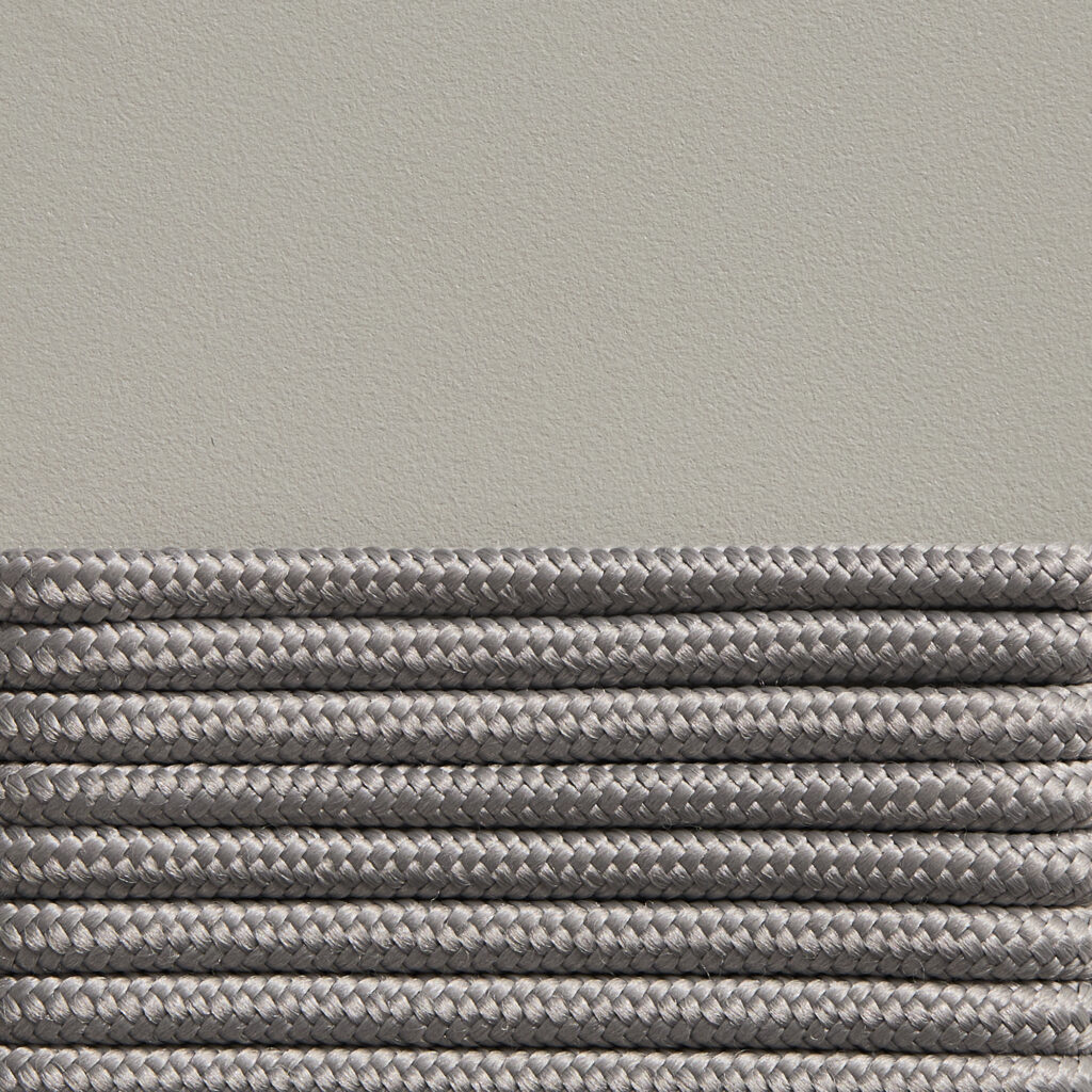 Des cordes tressées grises sont soigneusement alignées en rangées parallèles sur un fond beige, rappelant le design élégant d'un fauteuil Palissade CORD. Le jeu sophistiqué des teintes rouge fer et blanc crème complète l'ensemble.