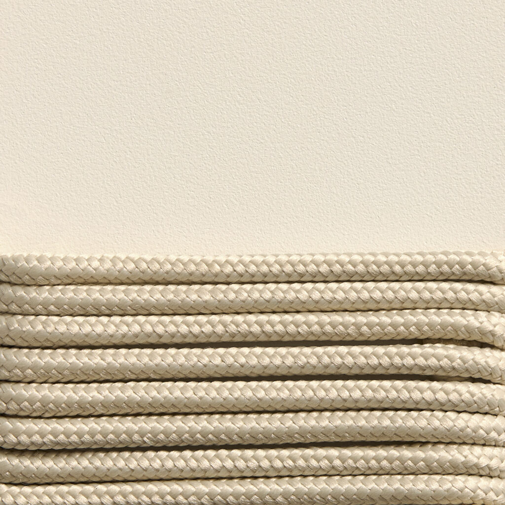 Gros plan de cordes tressées parallèles soigneusement empilées sur un fond texturé blanc cassé rappelant l'artisanat élégant que l'on retrouve dans une chaise longue Palissade CORD blanc crème.