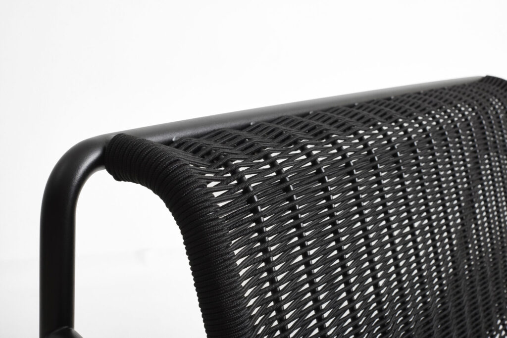 Gros plan sur une chaise au design tressé noir et à la structure métallique épurée, soulignant le motif et la texture complexes. Une touche de rouge fer ajoute de la profondeur, tandis que des touches de blanc crème offrent un contraste subtil, rappelant l'élégance du canapé lounge Palissade CORD.