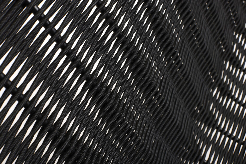 Gros plan sur un tissu noir tissé sur un canapé de salon, orné d'un motif entrecroisé. L'aspect texturé des lignes diagonales laisse passer la lumière, complétant à merveille les touches de blanc crème et de rouge fer.