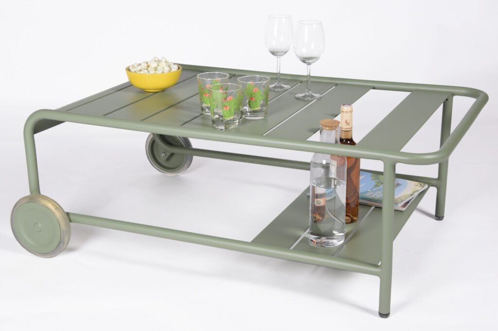 Un chariot roulant vert à roues rappelant un Luxembourg à roues contient des verres, des bouteilles de vin, un bol de pop-corn et un magazine sur le dessus.