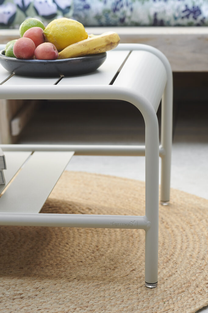 Un bol de fruits assortis, dont des bananes, des citrons, des pommes et des pêches, repose sur une table basse Carbone placée sur un tapis circulaire tissé.