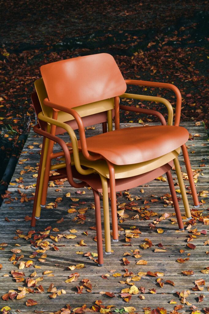 Trois chaises Fauteuil Lounge Studie orange et jaune empilées reposent sur une surface en bois parsemée de feuilles d'automne.